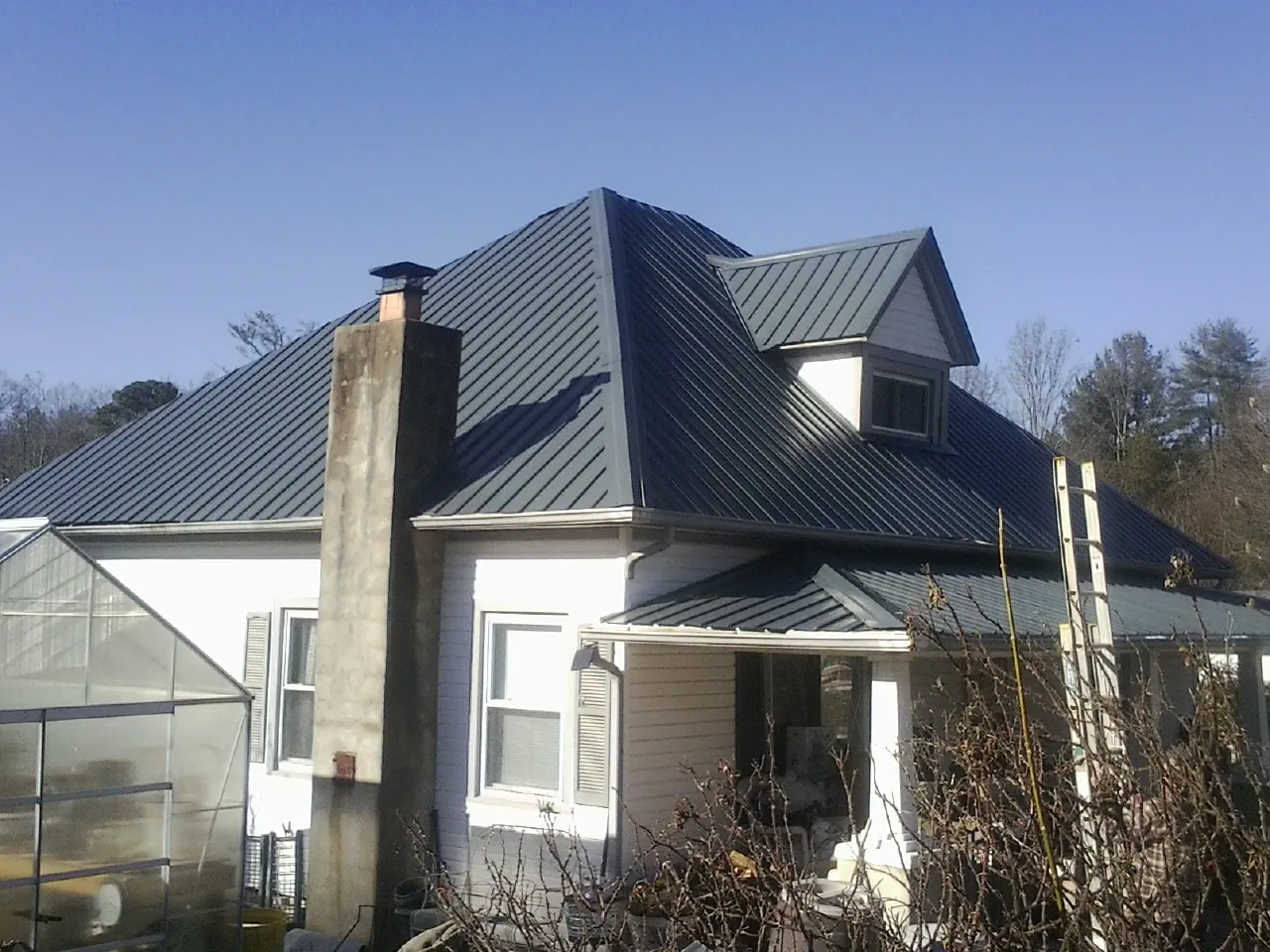 Dark blue standing seam metal roof on a white farmhouse with dormer — Slate & Tile Roof Repair by Roofing Brothers in Salemburg