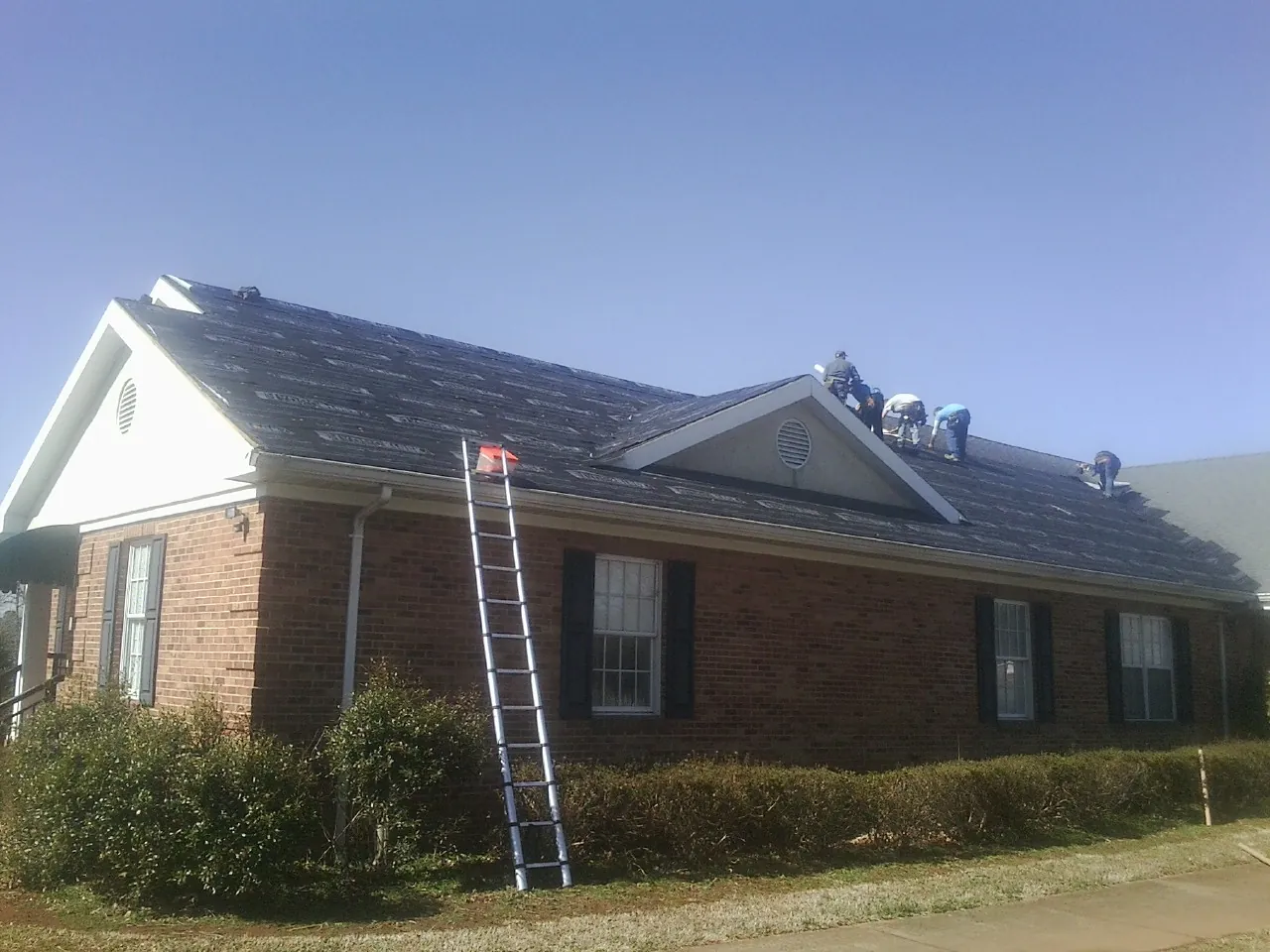 Crew tearing shingles off a brick ranch roof with a ladder set — Metal Roof Repair work by our crew in Salemburg