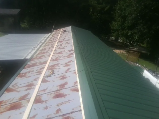 Old rusted panels beside newly installed green metal roofing — Wind Damage Roof Repair by Roofing Brothers in Salemburg