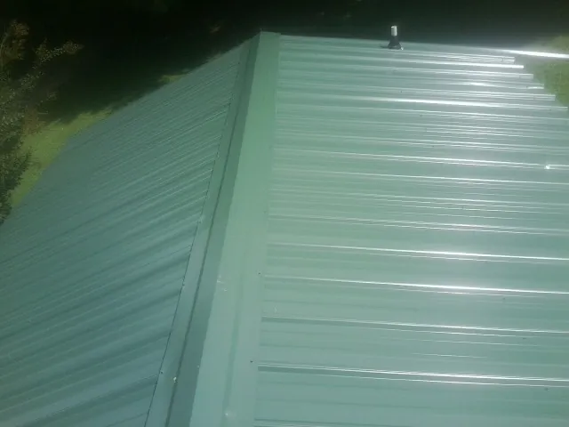 New green metal panels meeting at the ridge of a roof — Flat Roof Repair work by our crew in Salemburg