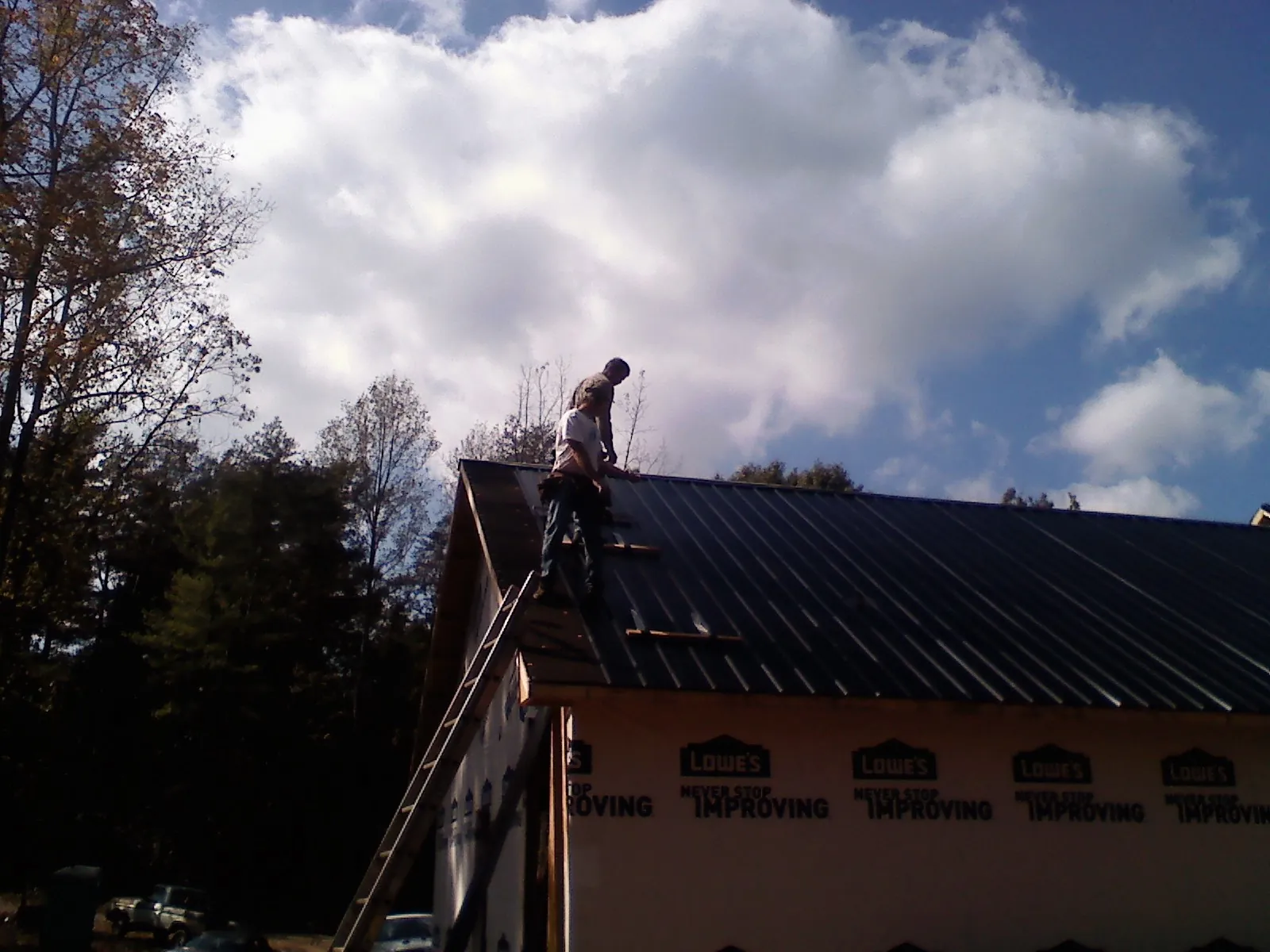 Roofer fastening dark metal panels high against a cloudy sky, from a Roof Inspection job in Salemburg