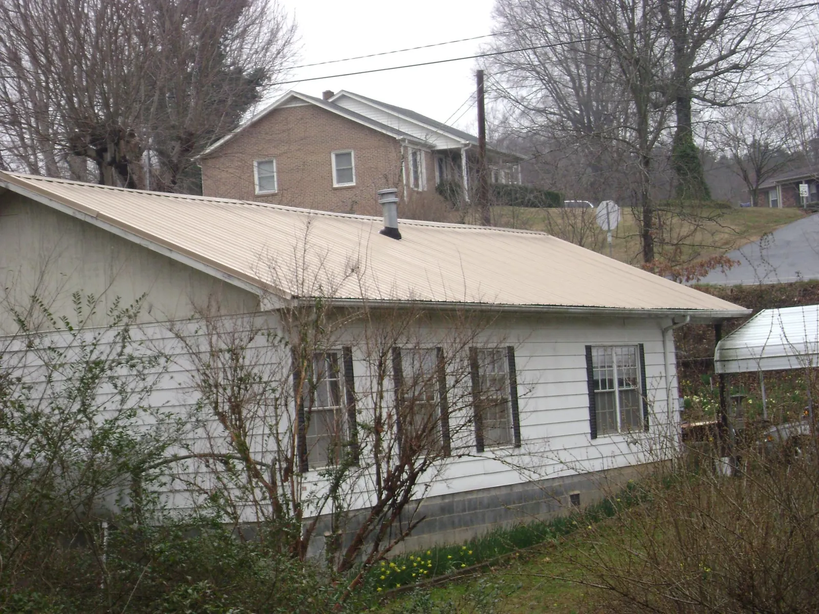 Tan metal roof on a white sided house set into a hillside — Commercial Roofing by Roofing Brothers in Salemburg